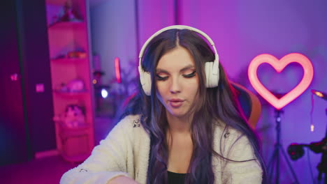 close-up portrait of young female programmer wearing headphone focused on computer work in colorful studio, briefly pauses to snack on popcorn before continuing