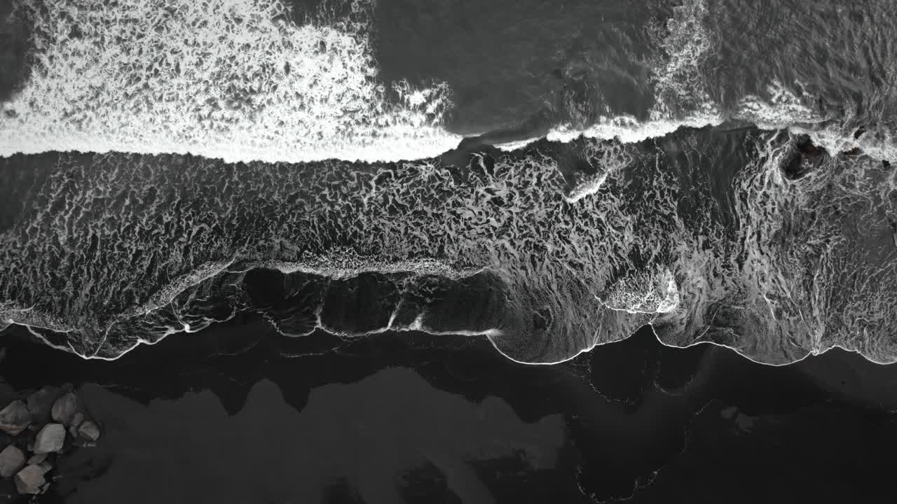 Aéreo cinematográfico de praia de areia preta, ondas quebrando na areia vulcânica, Islândia