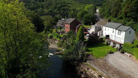 A-backwards-aerial-drone-shot-through-an-old-viaduct-in-South-Wales-with-a-beautiful-river-and-trees