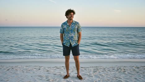 a young man enjoys a tranquil beach moment, strolling along the shore in a colorful floral shirt as the sun sets over the serene ocean landscape.