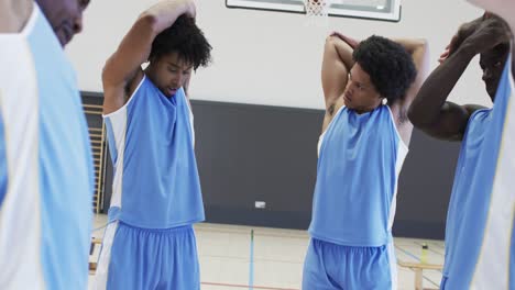 focussed diverse male basketball players stretching arms at training session, slow motion