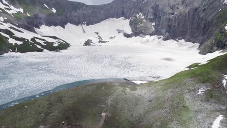 amplia vista del lago congelado de ratti gali, rodeado de escarpados acantilados nevados y verdes laderas alpinas