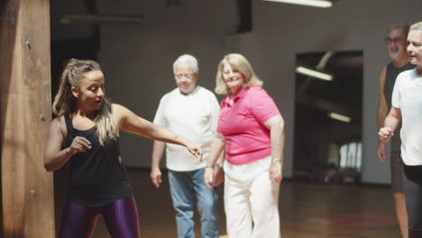 cheerful female teacher showing dance movements to senior people