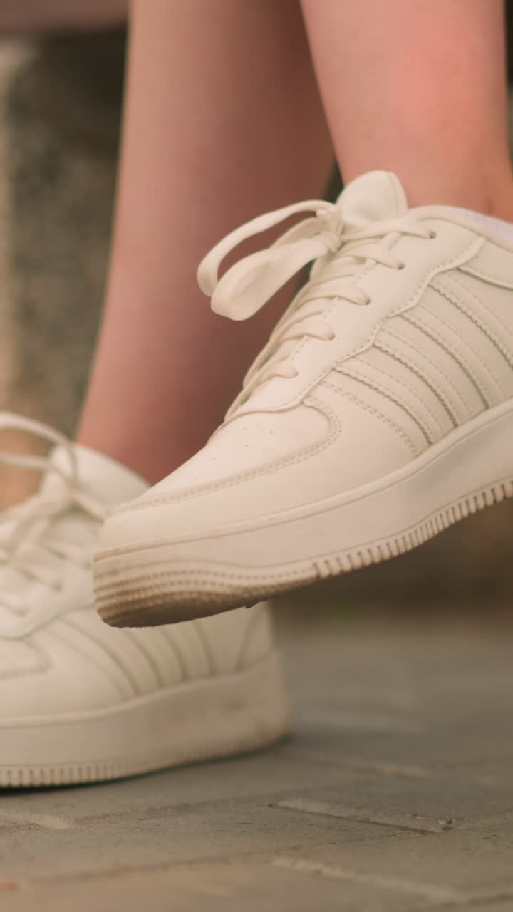 색 스니커를 입고 한 다리를 약간 들어 올려 야외에 앉아있는 백인 사람, 빛으로 부드럽게 조명 된 흐릿한 배경으로 다리의 부드러운 움직임