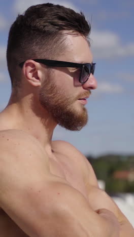 muscular athlete on the top of the hill. face of a bearded guy in black sunglasses outdoors on the blur city background. close-up. vertical video