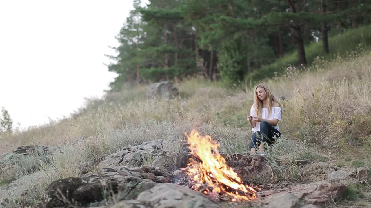 Young Woman Sitting Near Campfire. Young girl sitting near campfire in nature at evening