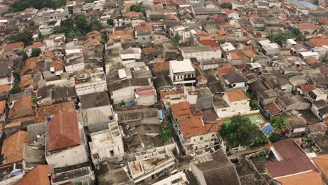 Aerial-top-down-shot-of-crowded-Indonesian-slum-with-amateur-soccer-field-during-sunny-day---Jakarta,-Indonesia