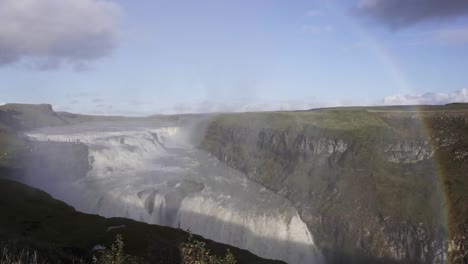 powerful foaming waterfall falling from slope with bright rainbow