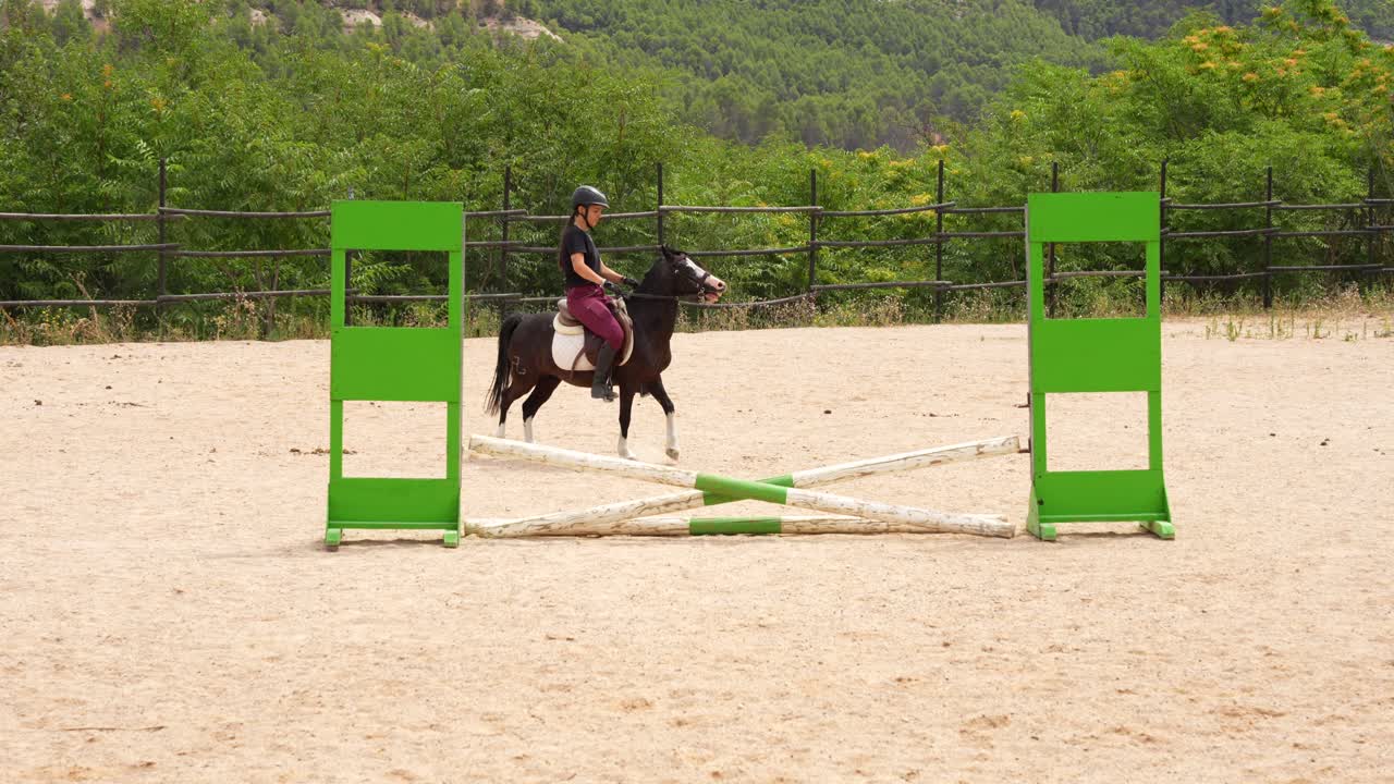 Female rider caressing her pony and walking in the track next to a hurdle