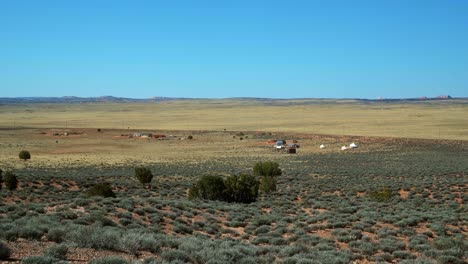 tilt up extreme wide landscape shot of a large desert plane used for sheep farming with small distant buildings and tents and the ground covered in sage brush in arizona on a warm sunny spring morning