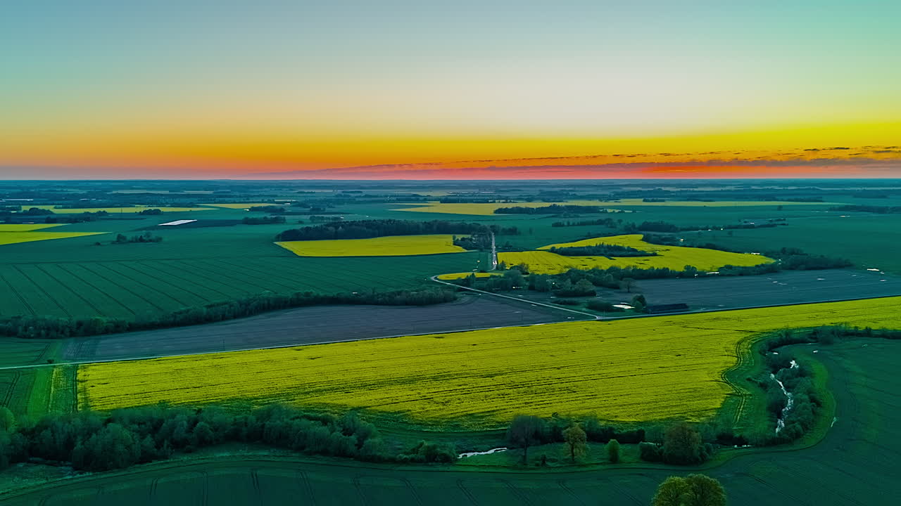 Patchwork farmland with green and yellow fields at dusk under colorful sky
