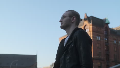 young european man with glasses, beard and man bun walking through city at golden hour shot at low angle