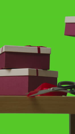 vertical video of man picking up pile of presents in gift wrapped boxes from table shot against green screen 1