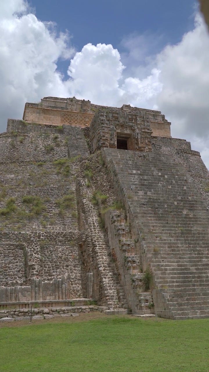 Inquadratura verticale statica dal basso dell'antica struttura della Piramide dell'Indovino nel sito archeologico di Uxmal nello Yucatan, Messico, sotto un cielo blu