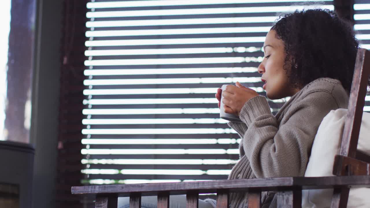African american woman drinking coffee while sitting near the fireplace at vacation home