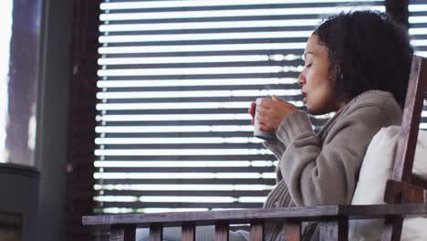 african american woman drinking coffee while sitting near the fireplace at vacation home
