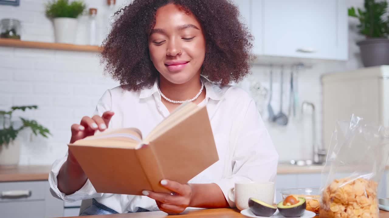 una atractiva mujer afroamericana hojea las páginas del libro y sonríe.