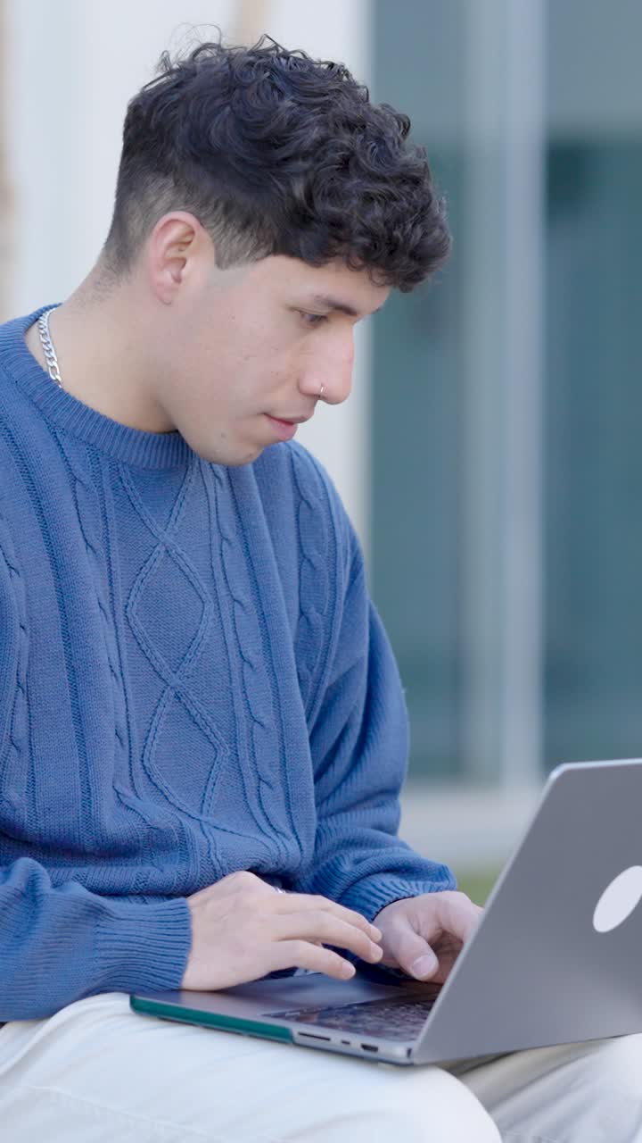 Young hispanic student typing on laptop computer. Vertical