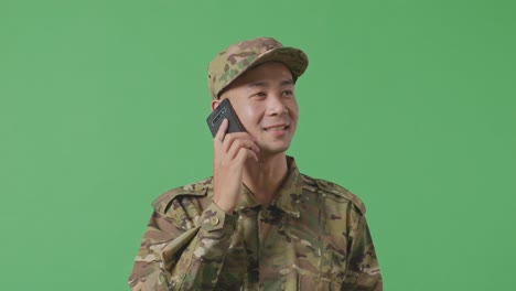 close up of asian man soldier talking on smartphone and looking around while standing in the green screen background studio