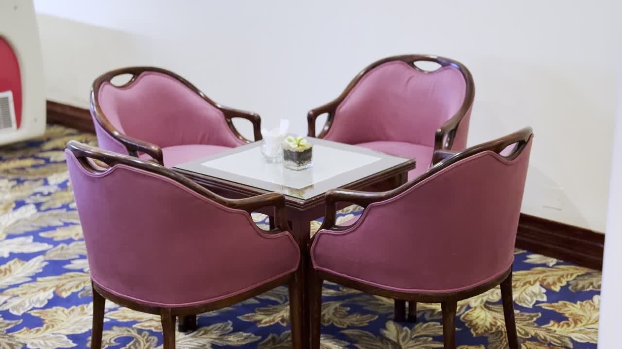Elegant seating arrangement with four plush red chairs and glass-top table on patterned carpet. Ideal for hospitality, interior design, or vintage decor content.