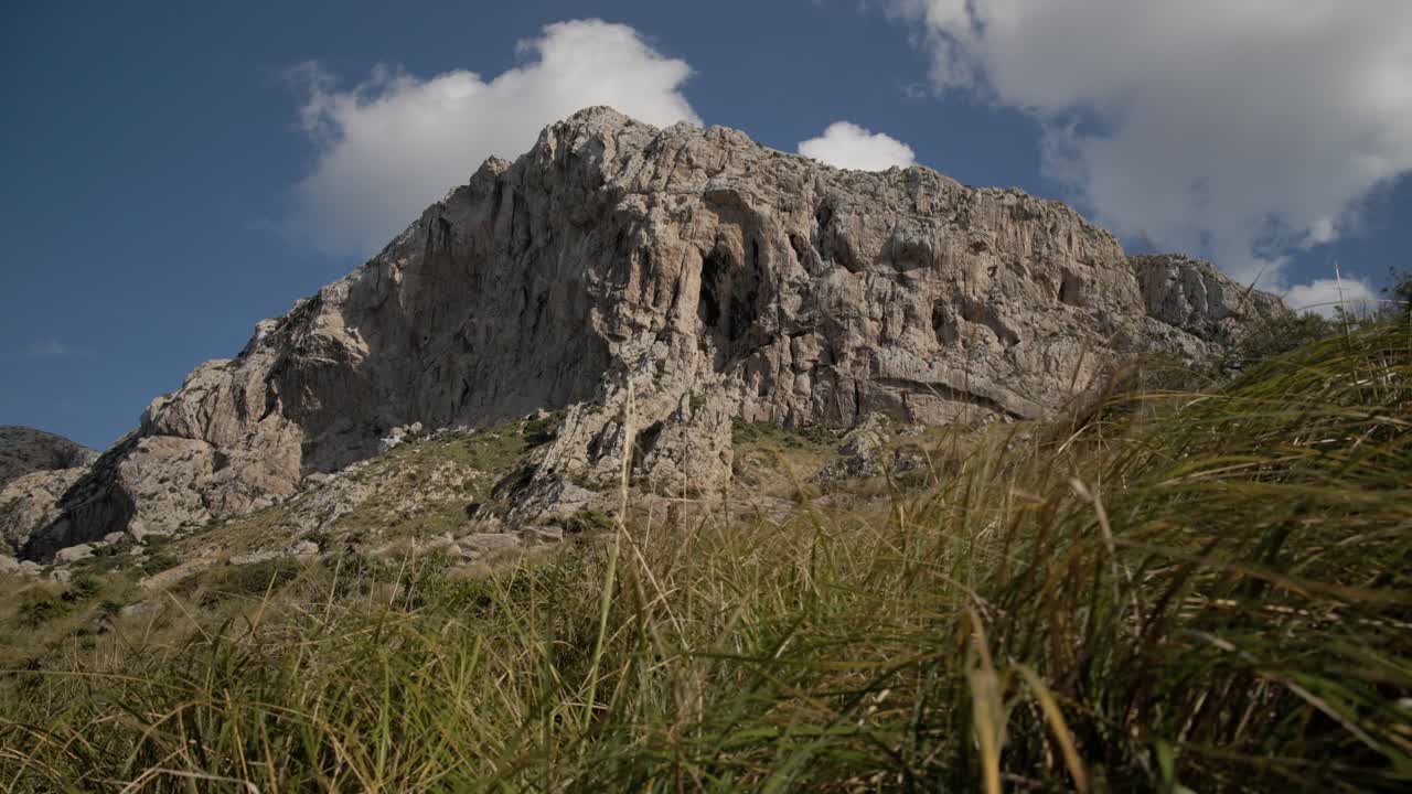 Mountain peak of Mallorca with grassy slopes and rocky ridges under bright summer sky, low angle establish of backdrop