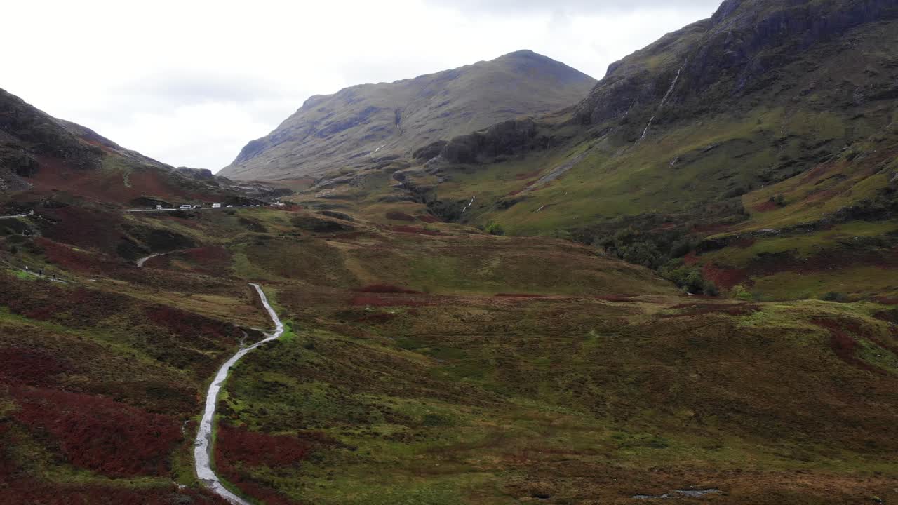 tiro aéreo hacia adelante mirando las montañas de glencoe escocia y el tráfico por carretera que pasa por