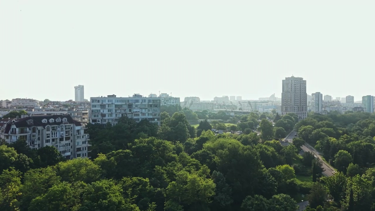 Vista do horizonte da cidade sobre árvores e parques verdes durante o dia, exibindo diversos edifícios e espaços abertos em um cenário urbano.
