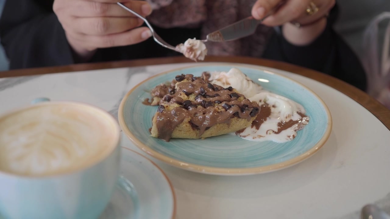 Primer plano de una persona comiendo postre de chocolate con helado y café.