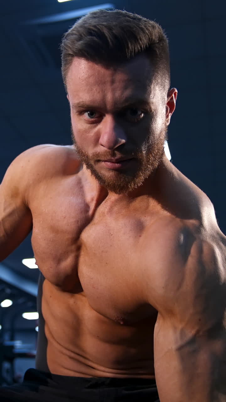 Handsome strong young bodybuilder work out with dumbbells. Strong abs. Modern gym background. Video from below. Vertical video