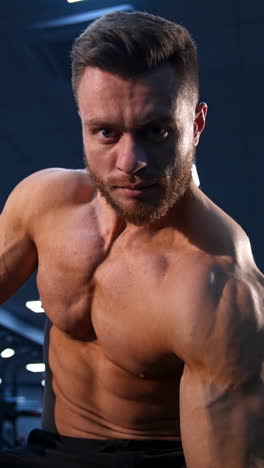 handsome strong young bodybuilder work out with dumbbells. strong abs. modern gym background. video from below. vertical video