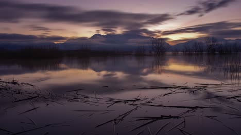 Lapso-De-Tiempo-De-La-Oscuridad-Al-Amanecer-De-Un-Lago-Con-Montañas-Nevadas-En-El-Fondo-Y-El-Cielo-Reflejándose-En-El-Lago---Alejar-Revelar