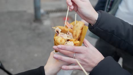 freshly fried street food in genoa, two people sharing a snack outdoors with wooden skewers