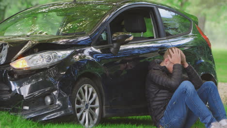 teenage driver with head in hands sitting  next to wrecked car after accident