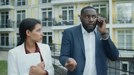 una pareja multiétnica molesta hablando por teléfono afuera.