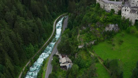 aerial view of torrente aurino river with pan up to reveal taufers castle in forested valley hills of south tyrol