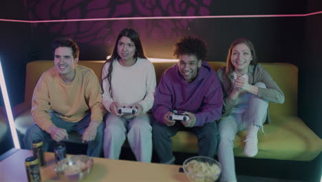 group of friends playing video games sitting on sofa at home 2