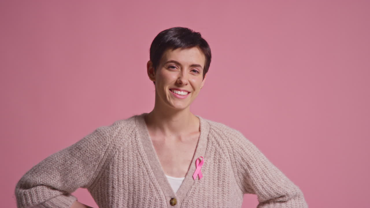 retrato de estudio de una joven sonriente que lleva con orgullo ropa rosa y una cinta de concienciación sobre el cáncer de mama contra un fondo rosa