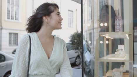 Young-woman-looking-at-shop-window-and-smiling