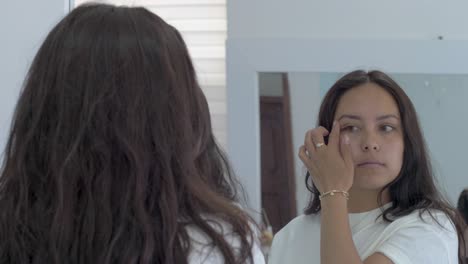 young-woman-looks-at-herself-in-the-mirror,-eyecontact,-checking-her-face,-pretty-look,-natural-beauty,-dark-hair,-female-face-medium-wide-reflection,-bathroom-mirrors,-make-up-eyebrow,-lashes-check