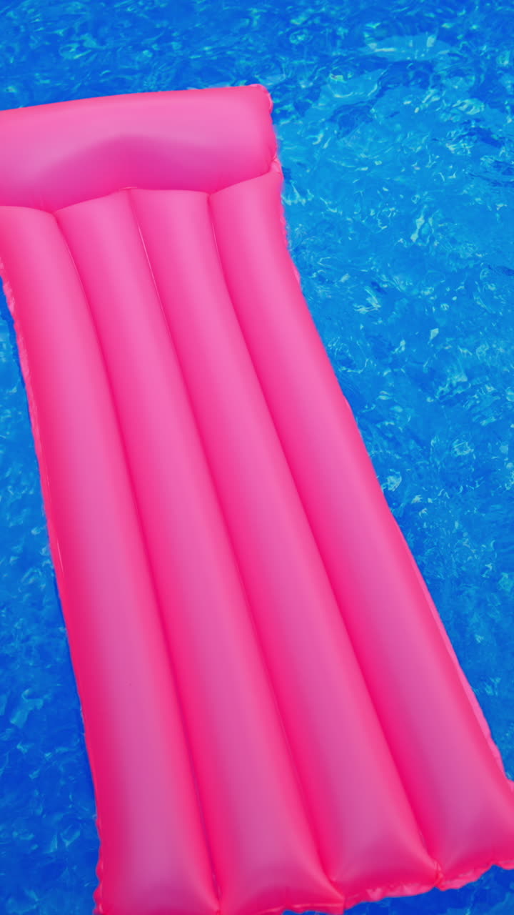 Long pink inflatable mattress in the blue water. Mattress drifting by the water in the swimming pool. View from top. Vertical video