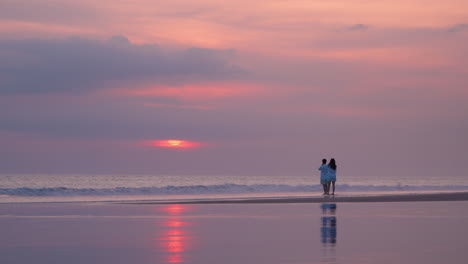 romantic couple at beach watching sunset and ocean waves in bali, indonesia