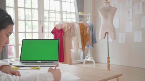 diseñadora asiática dibujando en papel con una pantalla verde en una computadora portátil