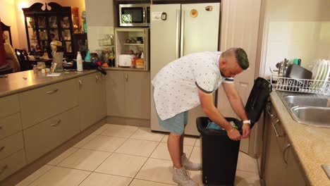 man in casual clothing emptying the kitchen garbage bin to put a bew bin liner in it