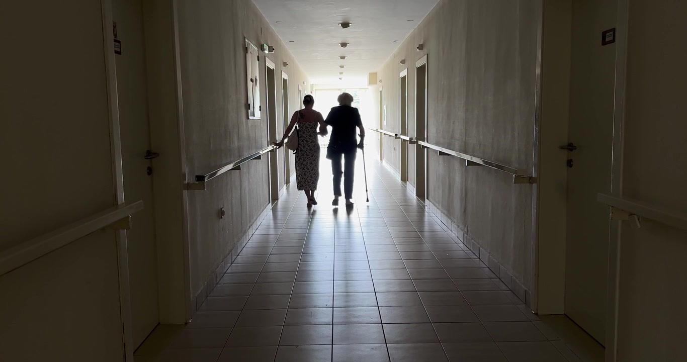 Donna anziana che cammina in un corridoio di una residenza per anziani con assistenza.