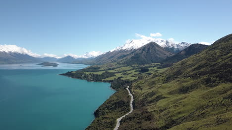 breathtaking aerial of crystal clear water on a paradise lake beside green rolling hills and a winding road through the mountains