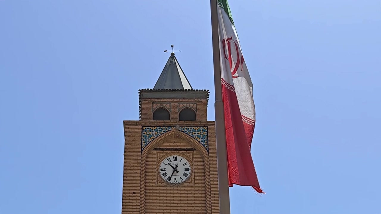 Bandiera dell'Iran che sventola accanto a una tradizionale torre dell'orologio in mattoni