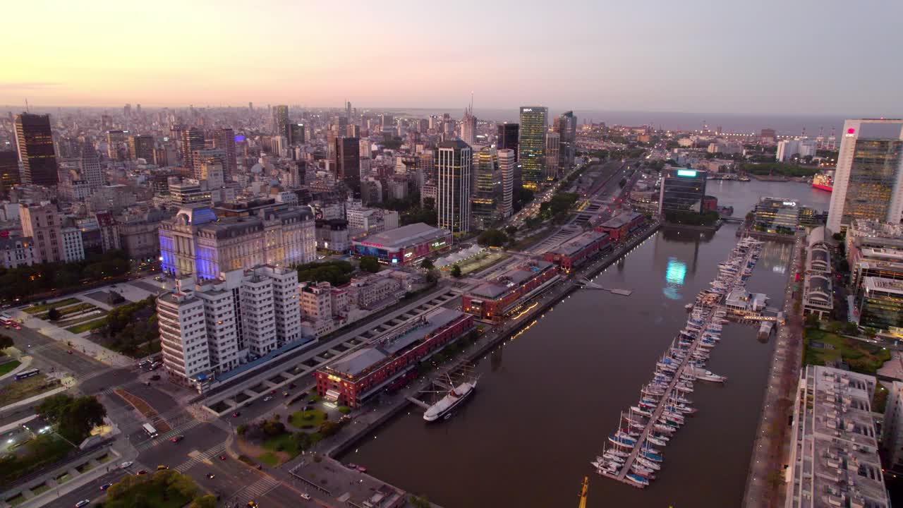vista aérea del carro de los muelles que actualmente tienen restaurantes de lujo y la entrada con el dique del río, hora azul con la ciudad y sus edificios iluminados en puerto madero