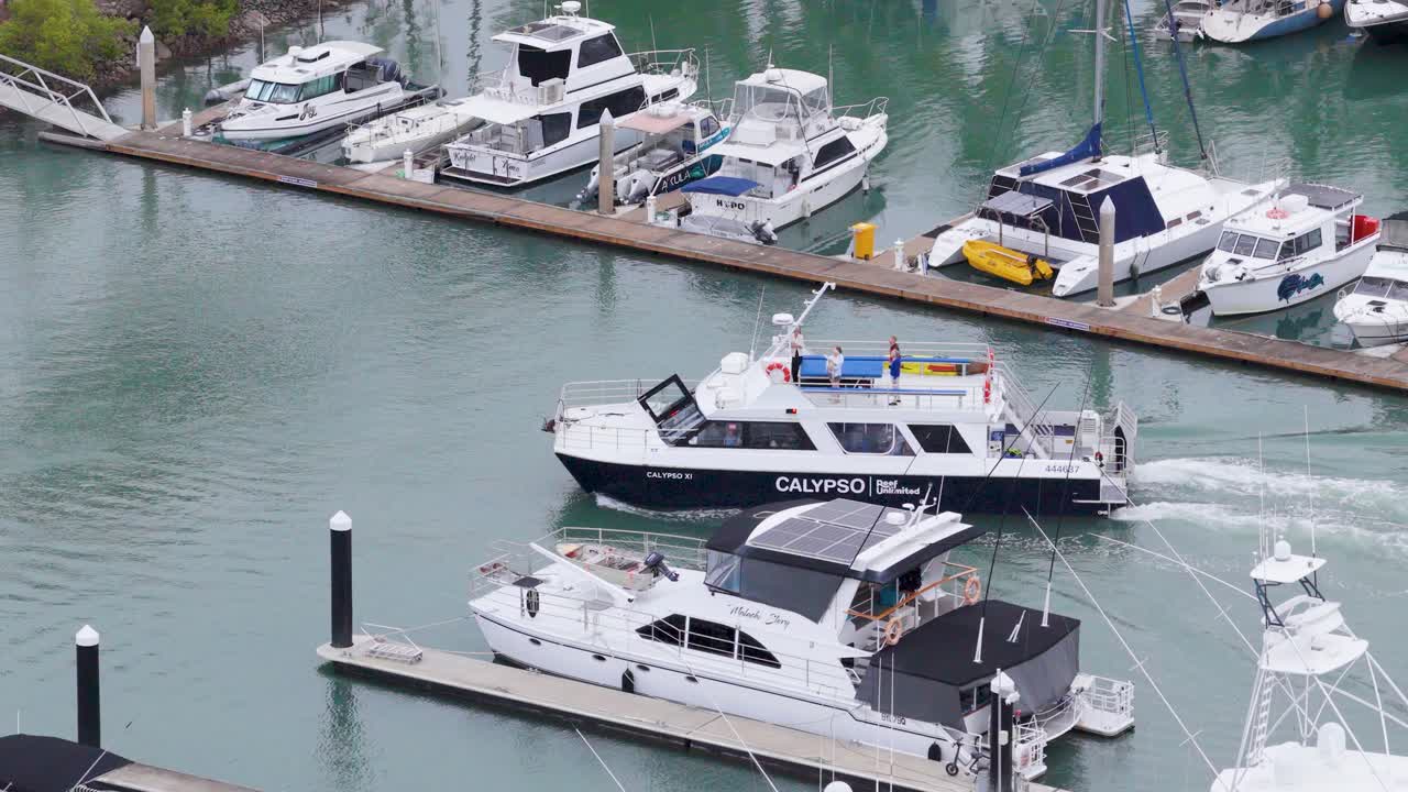 Aerial view of boats leaving a marina in Port Douglas, Australia. Calm waters, clear skies, and vibrant activity captured in daylight