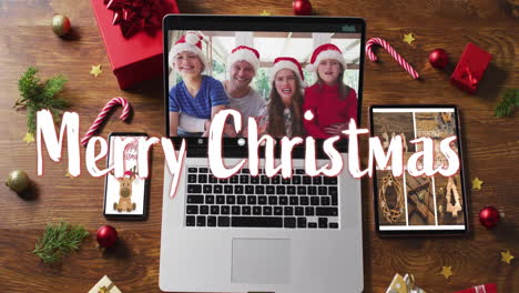animation of merry christmas text over decorations and caucasian family on laptop screen