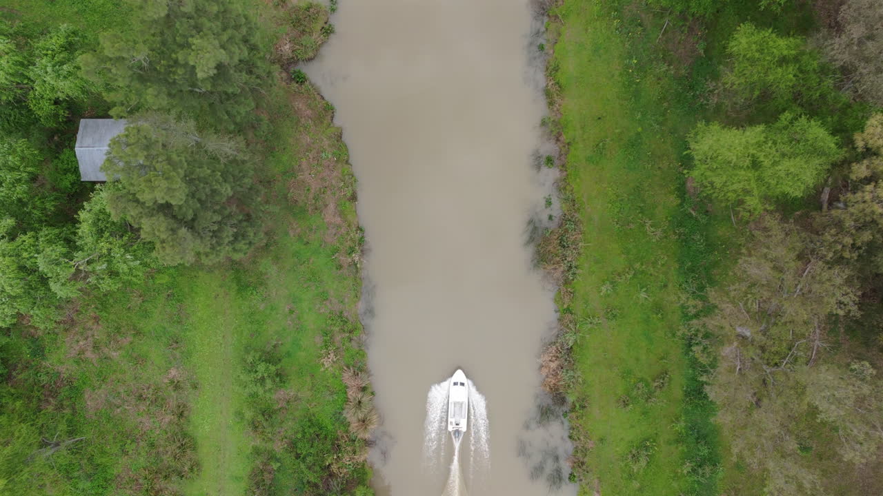 Motorboat moves slowly through narrow green river channel in subtropical wetland environment, top shot tracking